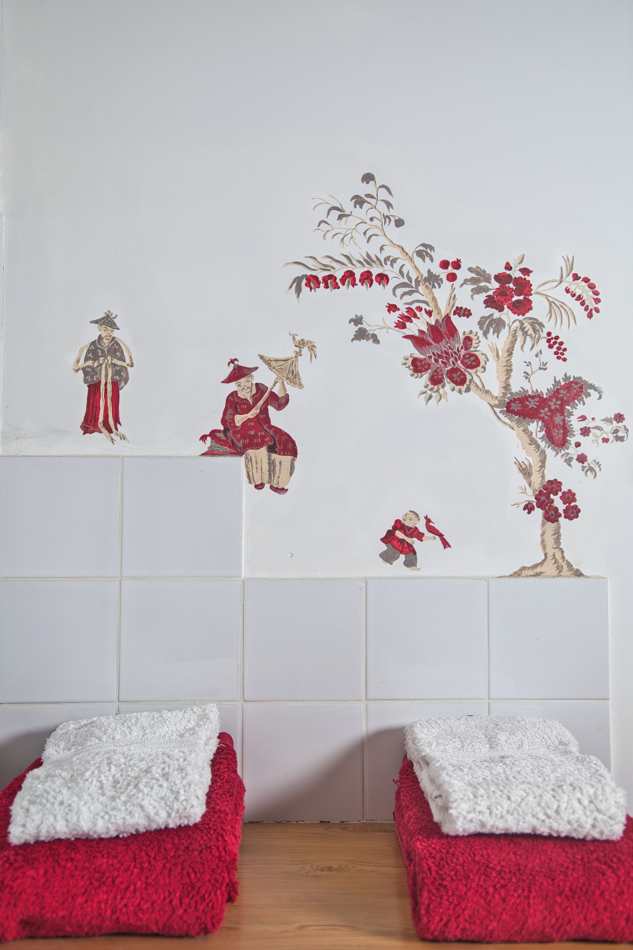 A bathroom with a tiled wall, two red towels, and a decorative wall piece.