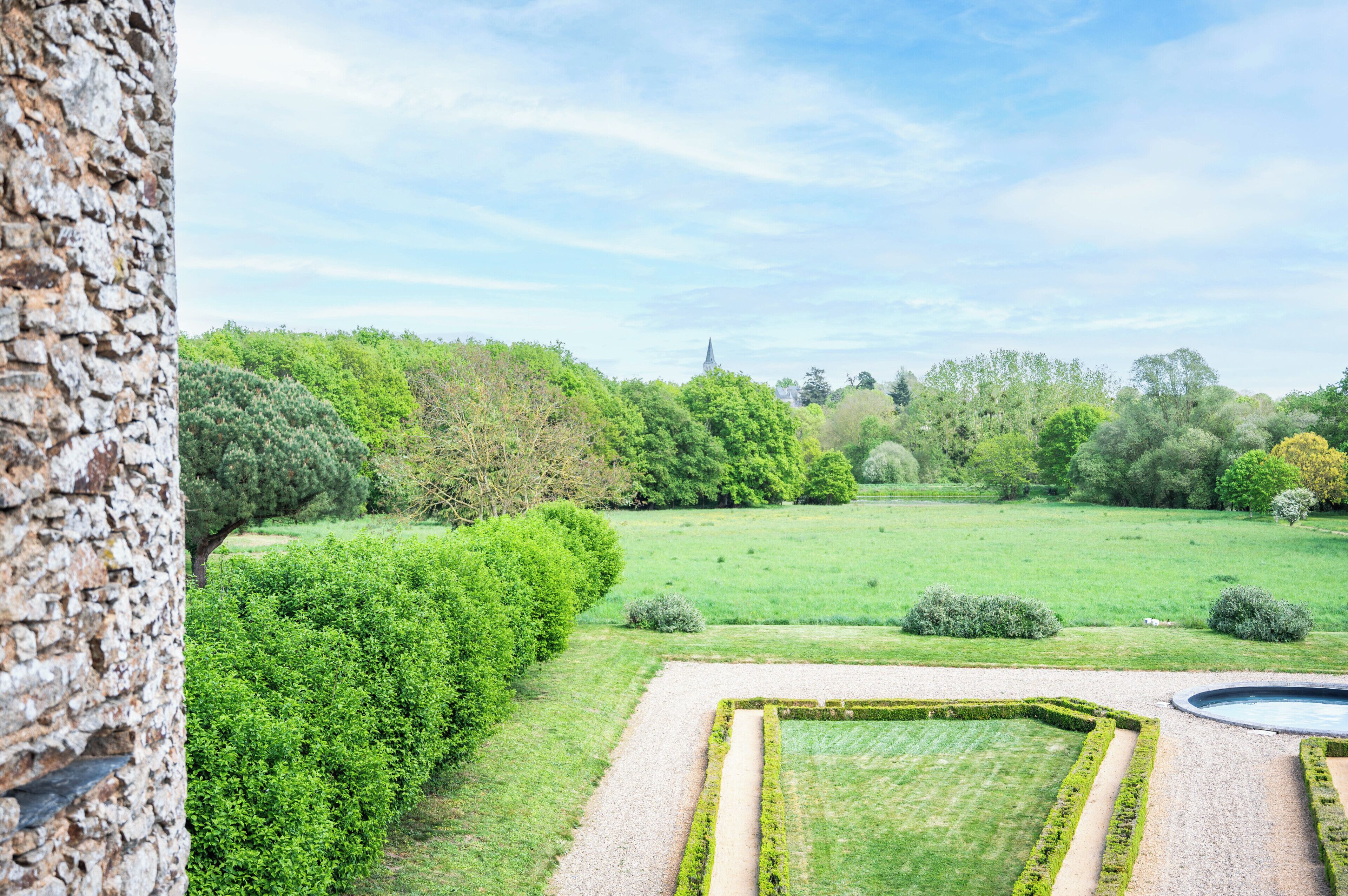 A landscaped garden with a hedge, a gravel path, and a circular water feature.