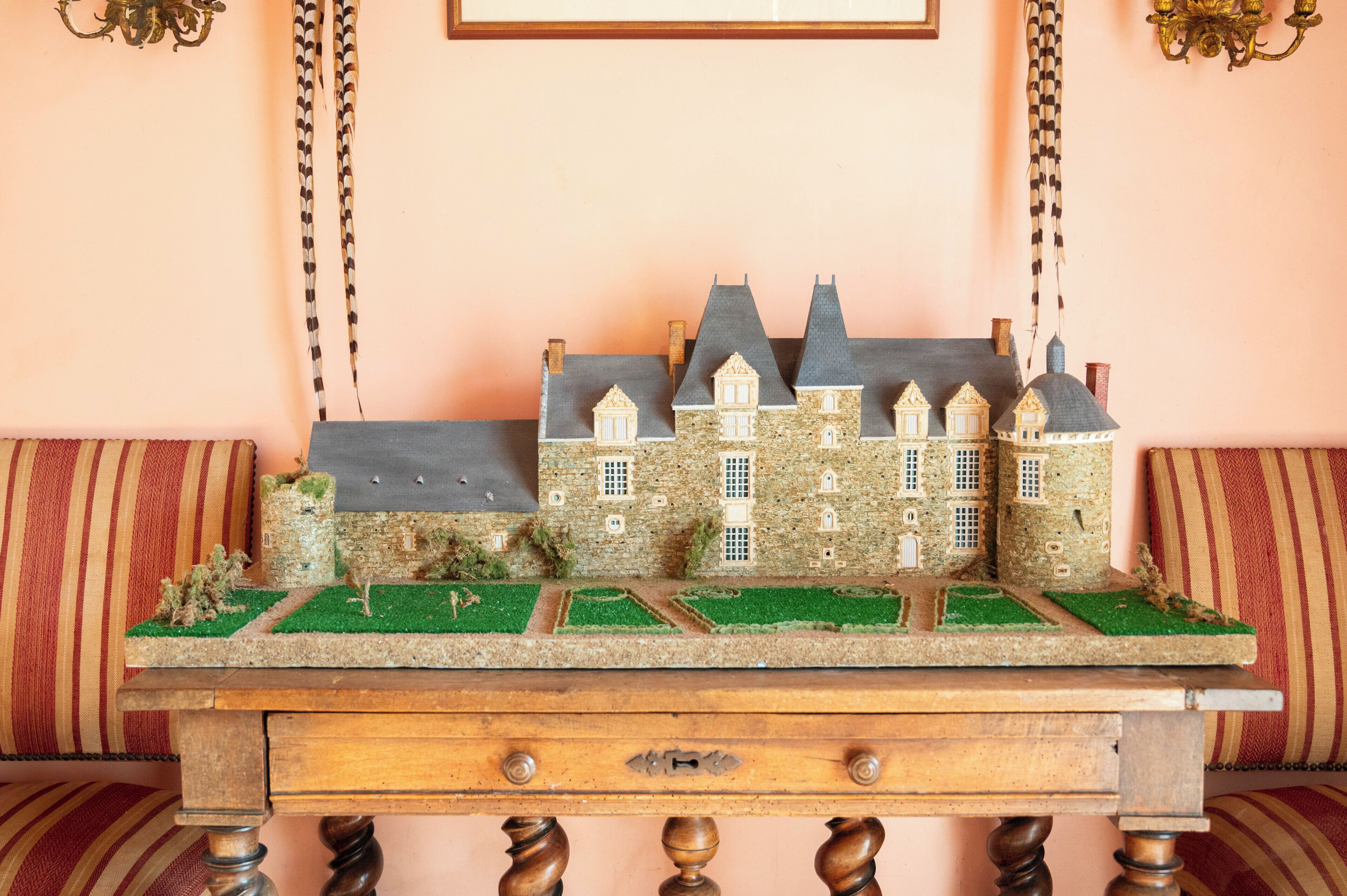 A model of a castle on a wooden table with a striped cushion in the background.
