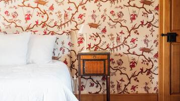 A bedroom with a bed, a nightstand, a lamp, and a floral wallpaper.