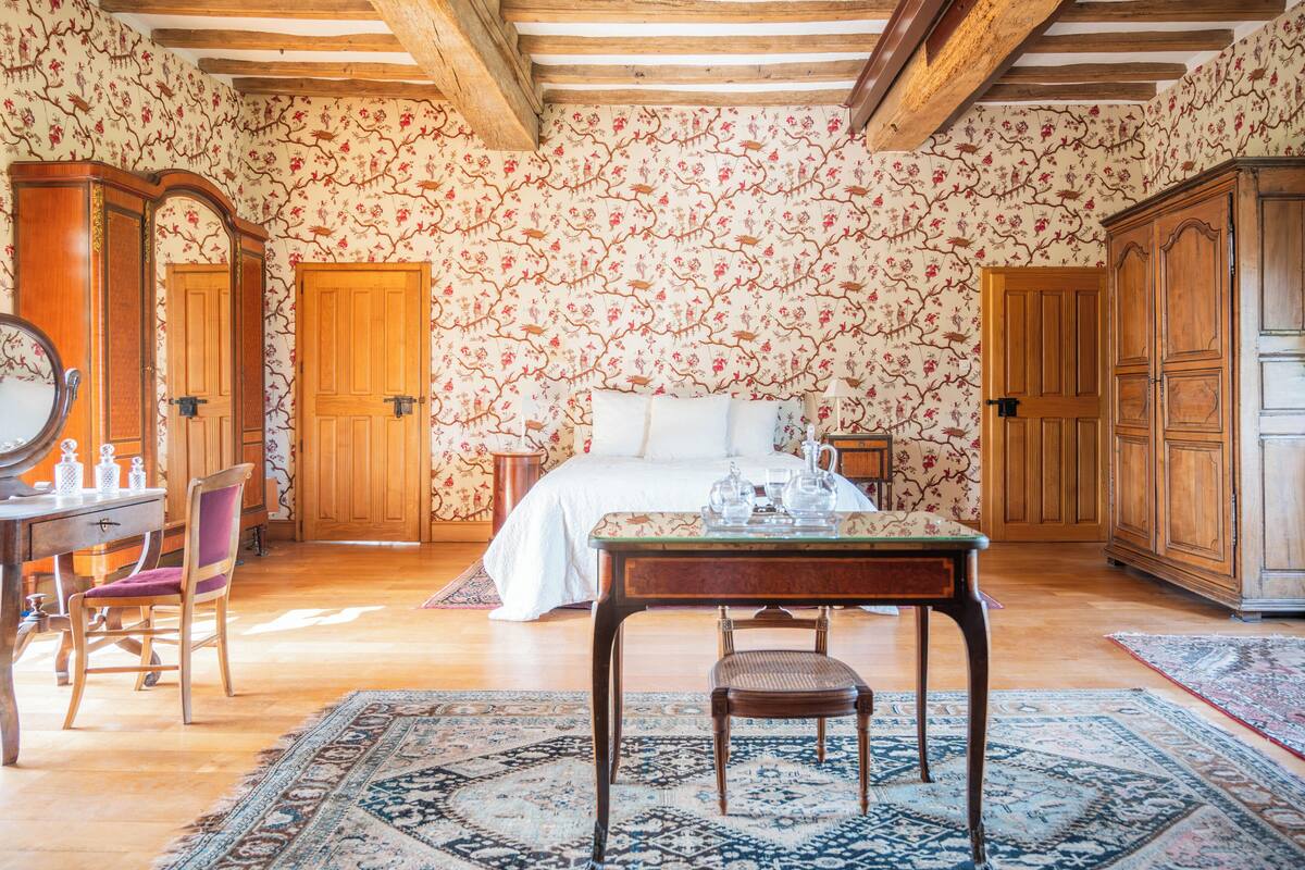 Una stanza con un letto, mobili in legno, un tavolo con teiere e carta da parati a motivi floreali.