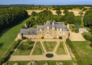 A large stone castle with multiple towers, surrounded by well-manicured gardens and a moat.