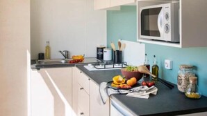A modern kitchen with white cabinets, a black countertop, a microwave, and a potted plant. - Camping 3 étoiles - Piscine  - ccbfgbf (Collias)