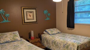 Un dormitorio con dos camas individuales, un ventilador de techo, un cuadro enmarcado y una ventana con cortinas.