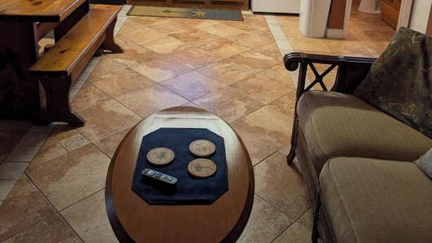 Cocina compacta con microondas, estufa y refrigerador. Hay una mesa de comedor con un banco y una pequeña mesa redonda con un control remoto.