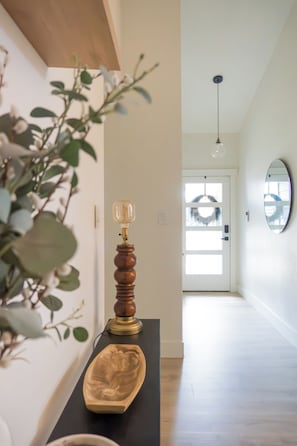 Un couloir doté d’un plancher en bois, d’une console noire surmontée d’une lampe, d’un miroir et d’une plante.