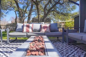 An outdoor seating area with a sofa, a fire feature, and a patterned floor. - A Cozy Retreat | Near Austin | Pet Friendly (Cedar Park)