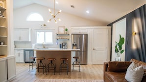 A modern kitchen with white cabinetry, a central island with stools, a stainless steel refrigerator, and a bar area. - Cozy 3BR/2BA - Peaceful, Pet-friendly Home (Cedar Park)