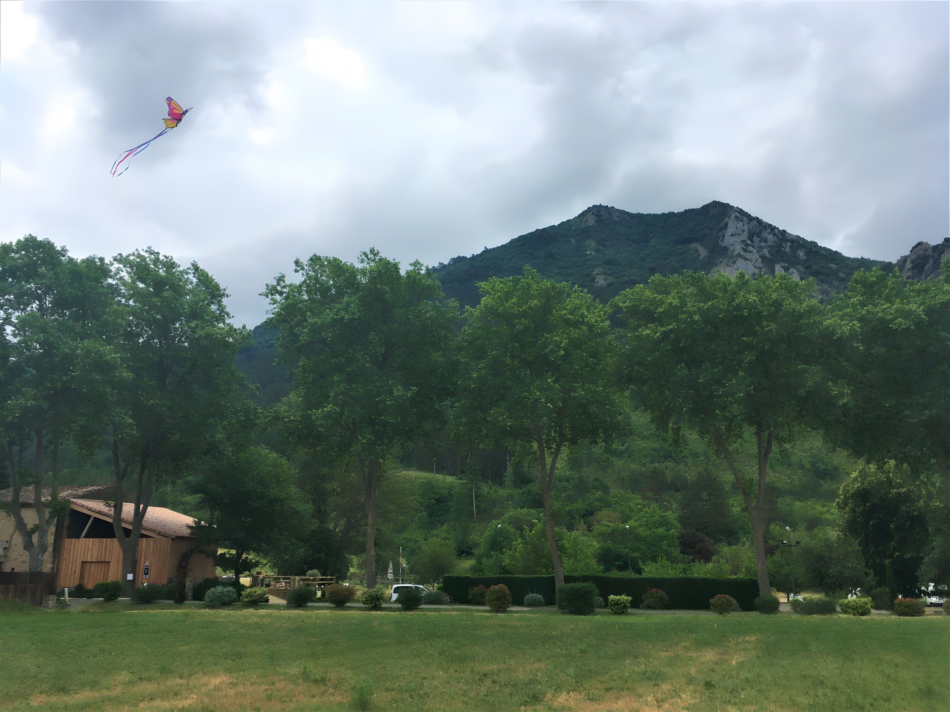 Un campo cubierto de hierba con una montaña al fondo y un edificio de techo inclinado.