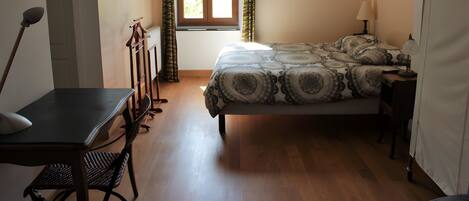 A bedroom with a bed, a desk, a chair, a lamp, and a window with curtains.