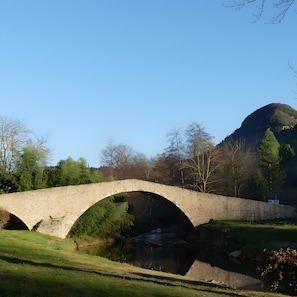 A stone bridge over a river with a mountain in the background.