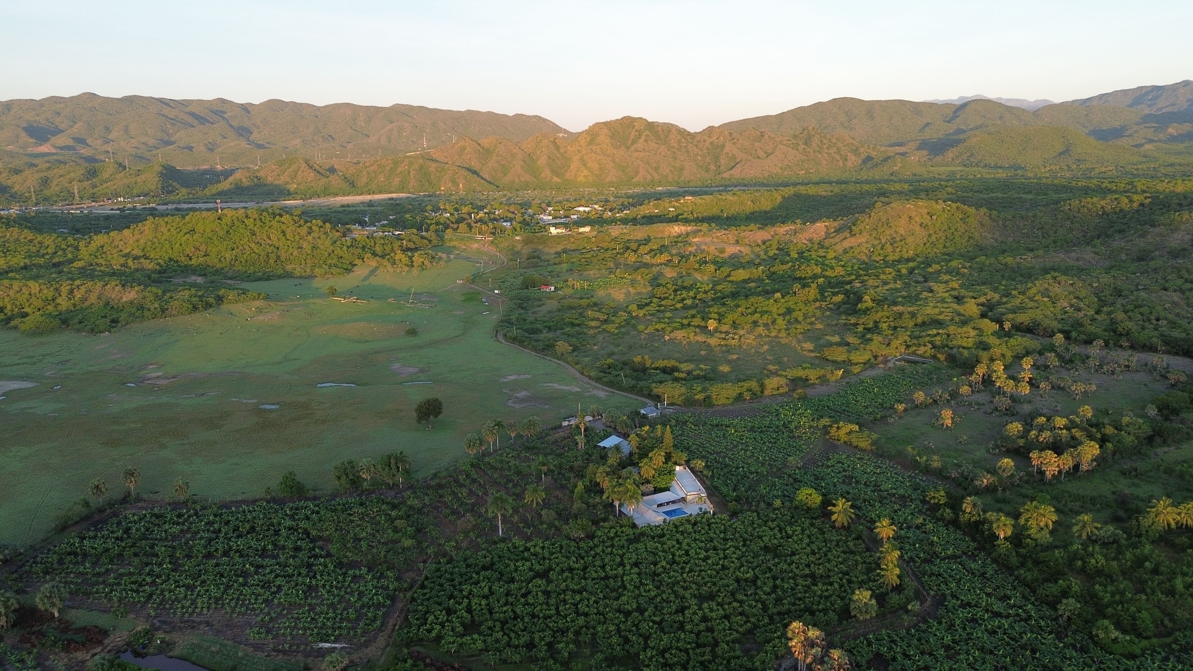 An aerial view of a rural landscape with a golf course, dense vegetation, and distant mountains.