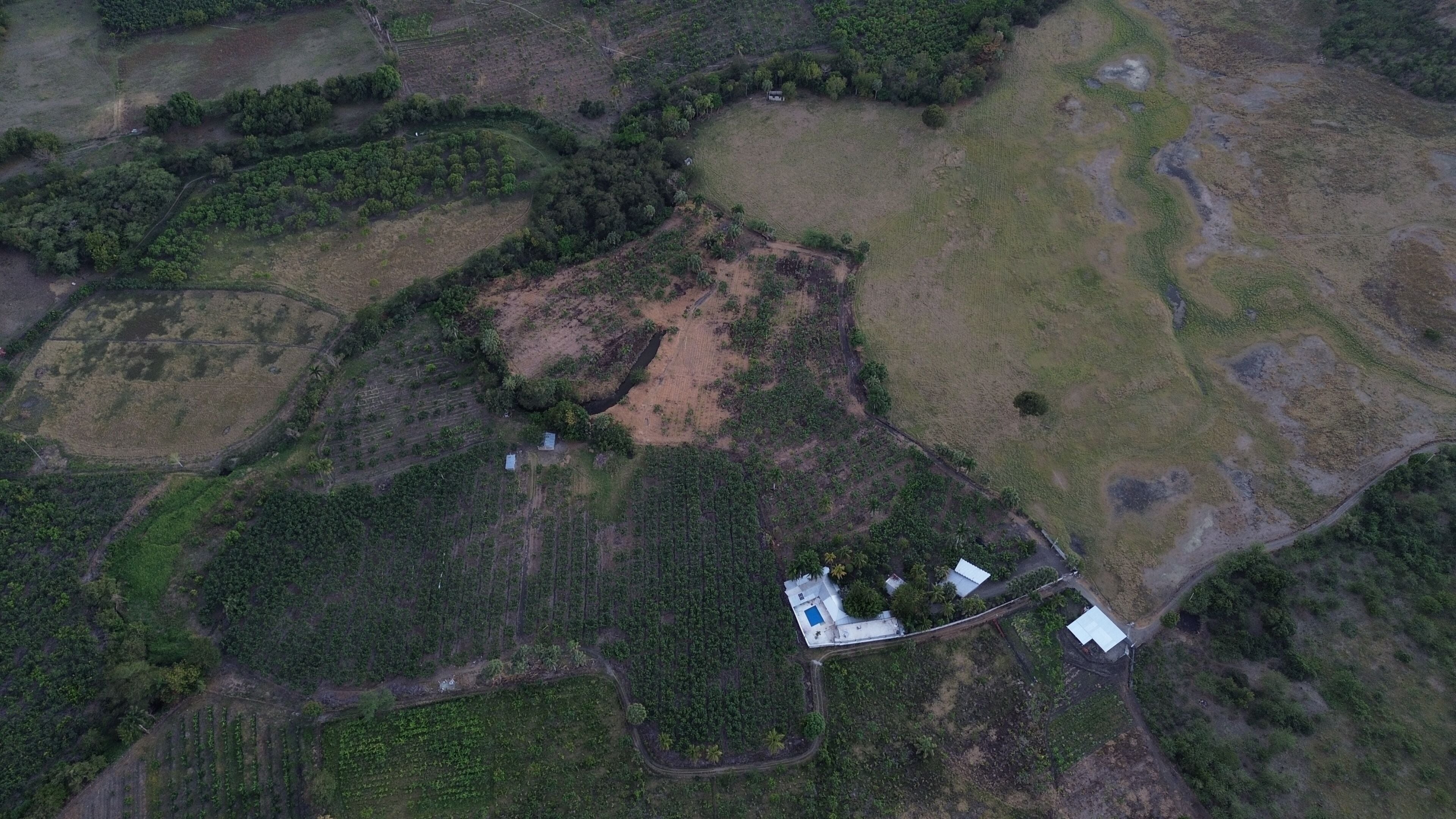 An aerial view of a rural property with fields, a small house, and a swimming pool.