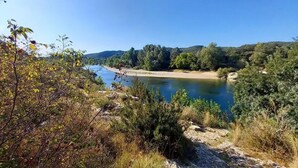 Ein Fluss mit einem Sandstrand, umgeben von dichtem Grün und Hügeln im Hintergrund.