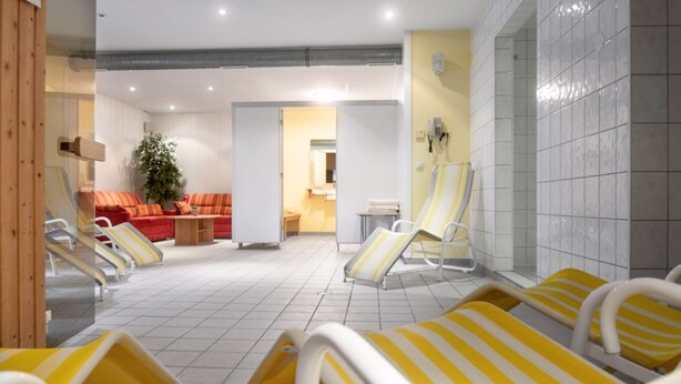 Een wellnessruimte met ligbedden, een rode bank en een plant.