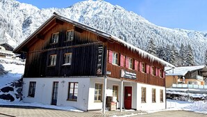 Een houten gebouw met een rode deur, een bord met daarop 'living store' en besneeuwde bergen op de achtergrond.