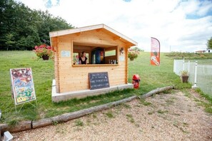 Eine kleine Holzhütte mit einem Schild, wahrscheinlich ein Imbissstand, in einer grünen, offenen Umgebung.