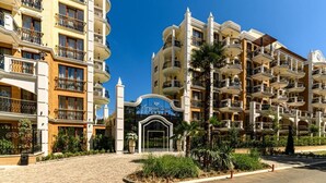 A multi-story hotel with balconies, a central entrance, and surrounding greenery. - Sunny Beach resort apartment with sunny balcony, pools & spa near beach (Sunny Beach)