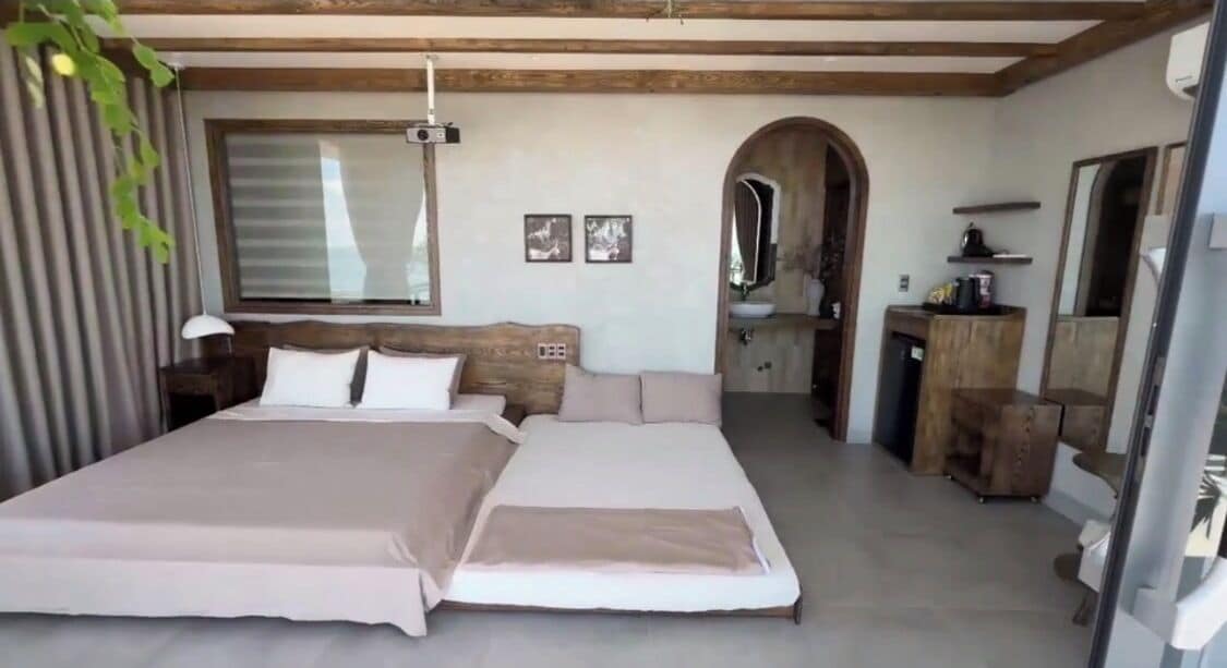 A bedroom with a large bed, a wooden headboard, a mirror, a small desk, and a window.