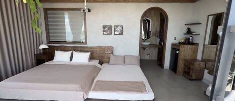 A bedroom with a large bed, a wooden headboard, a bedside table, a mirror, and a small kitchenette area.