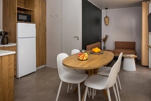 Eine moderne Küche mit weißen Schränken, einer Mikrowelle und einem Kühlschrank. Es gibt einen Essbereich mit einem Holztisch und weißen Stühlen.