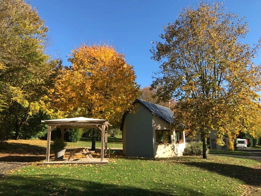 Un kiosque, un petit abri et un arbre aux feuilles jaunes, le tout situé dans un espace verdoyant.