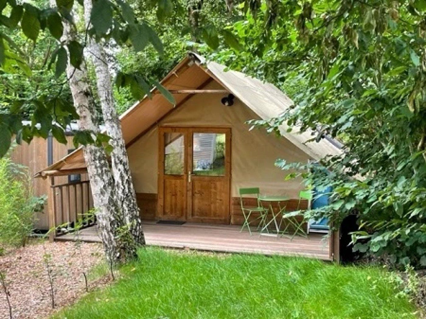 Een houten hut met een schilddak, een voordeur en een klein terras met stoelen.