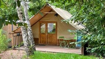 Een houten hut met een schilddak, een voordeur en een klein terras met stoelen.