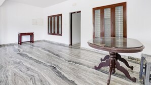 Ein geräumiges Zimmer mit Marmorboden, einem runden Holztisch und zwei Türen mit satinierten Glasscheiben.