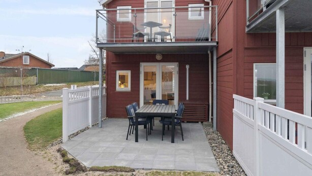 Uma casa de dois andares com varanda, um pátio com mesa e cadeiras e um quintal cercado.