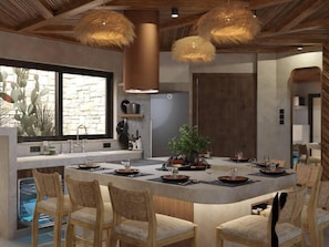 A modern kitchen with a central island, wooden chairs, and pendant lighting. - Sperveri Terra Incognita (Afandou)