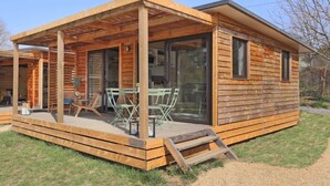 En træhytte med en overdækket terrasse, glasdøre og et spiseområde med udendørs møbler.