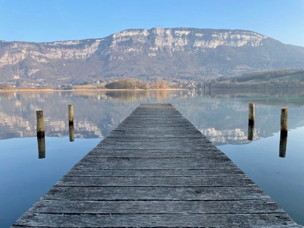 Une jetée en bois s’étendant sur une étendue d’eau calme, avec une montagne en arrière-plan.