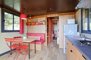 A compact kitchen with a dining area, a kitchenette, and a small seating area with a red sofa and table. - Camping 3 étoiles - ccbfgh0 (Lépin-le-Lac)