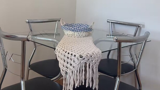 Ein Essbereich mit einem Glastisch, schwarzen Stühlen und einer Wanddekoration aus Fransenknäueln.