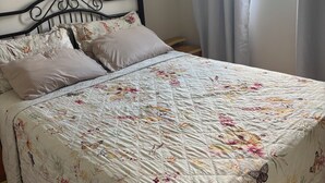 Ein Bett mit blumigem Bettbezug, einem Kopfteil und einem Fenster mit Vorhängen.