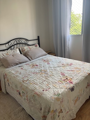 Una cama con ropa de cama estampada, cabecera y ventana con cortinas.