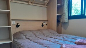 Un letto con copriletto trapuntato, una testiera con due lampade a parete e una finestra con tenda.
