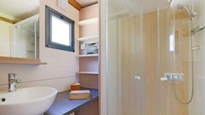 Un bagno con un lavandino bianco, uno specchio, una doccia e una finestra.