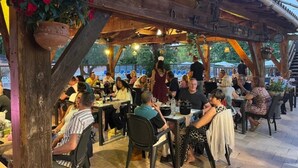 Area pranzo all'aperto con tavoli e sedie in legno, circondata da una struttura in pergolato di legno.