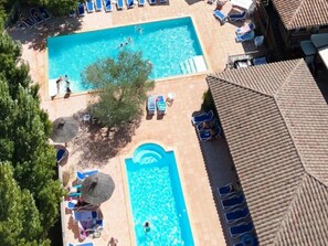 Ein Pool mit Liegestühlen und Sonnenschirmen, umgeben von Bäumen und Gebäuden.