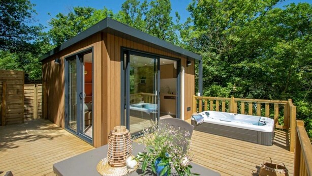 A wooden deck with a hot tub, a glass-enclosed room, and a table with a candle and flowers. - Chalet 4 étoiles - Piscine  - ccbehhg (Saignon)