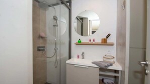 A modern bathroom with a glass-enclosed shower, a round mirror, a white sink, and a wooden shelf with toiletries. - Chalet 4 étoiles - Piscine  - ccbehhg (Saignon)