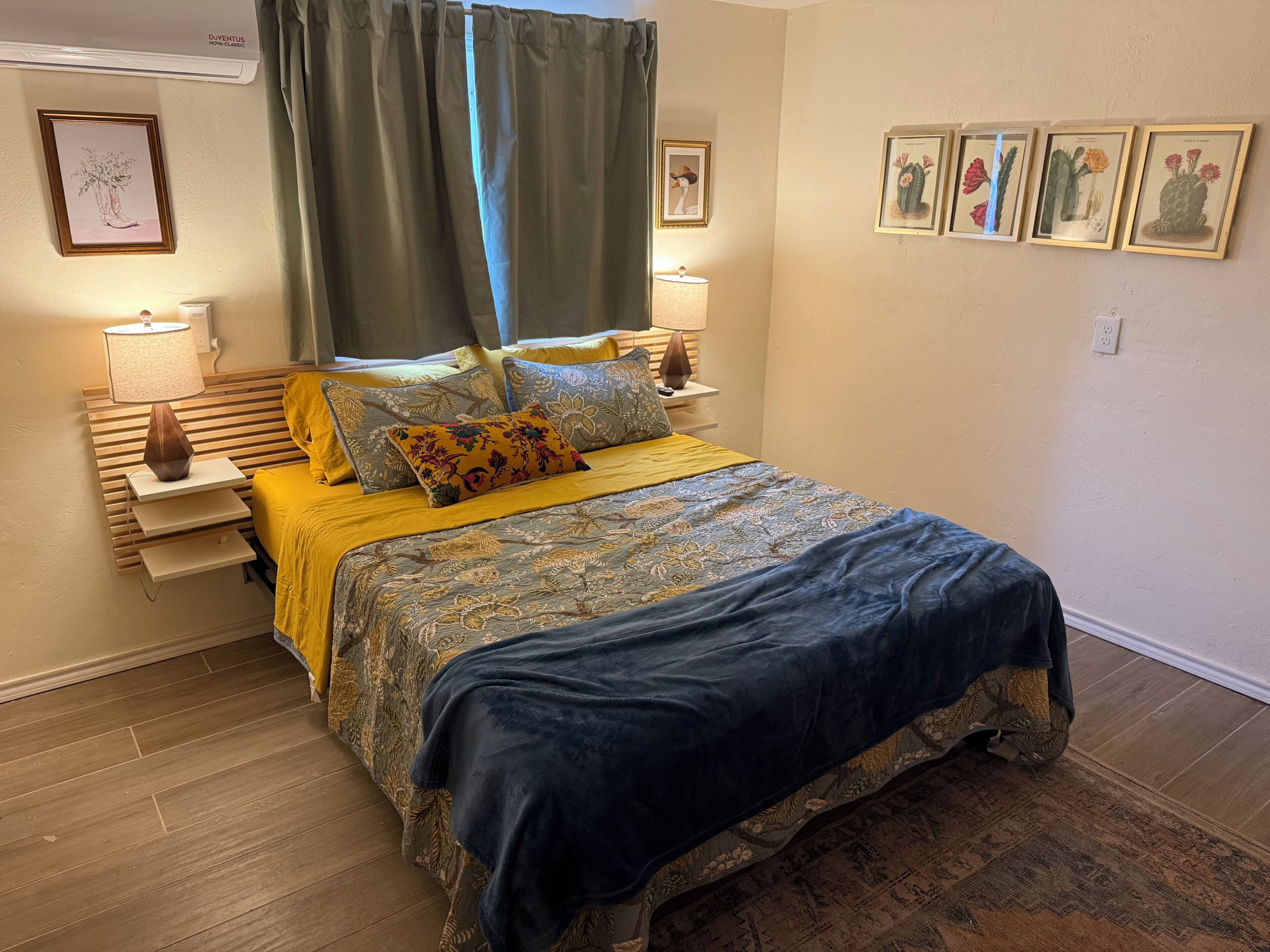 A bedroom with a bed, bedside tables, lamps, and framed botanical prints on the walls.