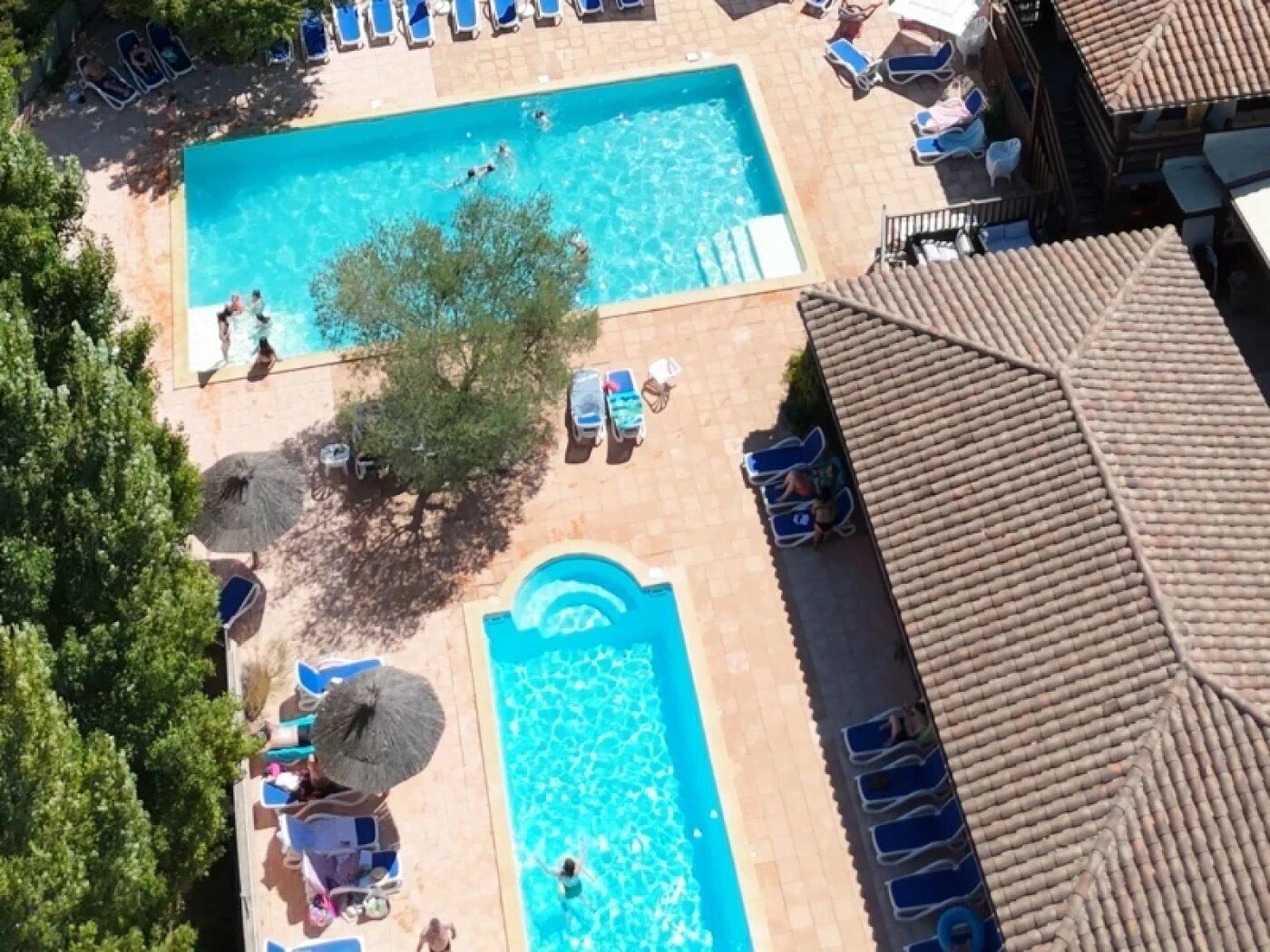 Piscina com espreguiçadeiras e guarda-sóis, rodeada por árvores e um telhado telhado.