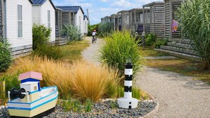 A row of mobile homes with a gravel path, a small boat model, and a lighthouse model. - Camping 3 étoiles - Piscine  - ccbffbc (Saint-Denis-d'Oléron)