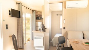 A compact room with a bed, a dining table with chairs, a TV mounted on the wall, and a kitchenette area. - Camping 3 étoiles - Piscine  - ccbffbc (Saint-Denis-d'Oléron)
