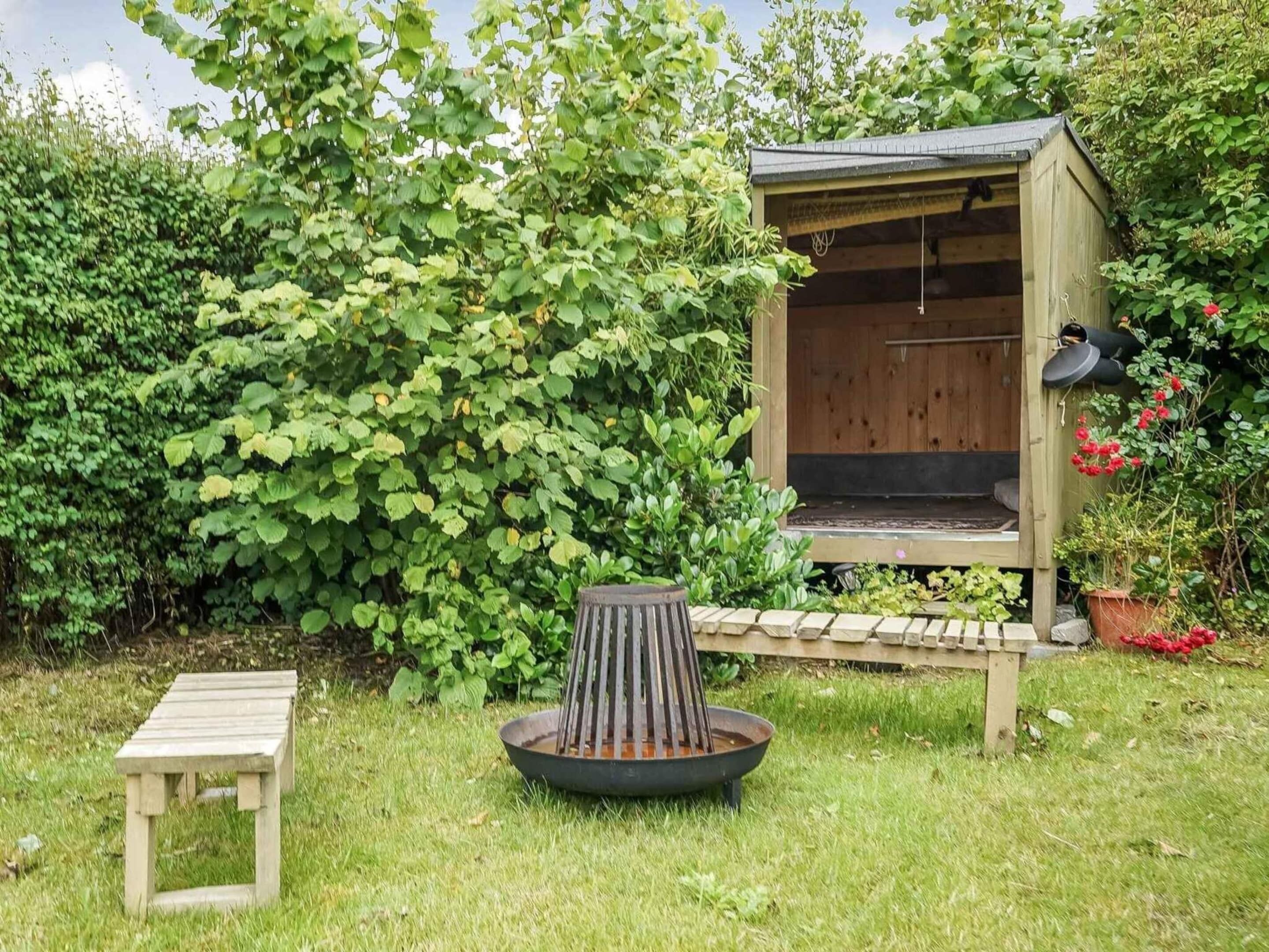 A wooden outdoor seating area with a fire pit, a small table, and a wooden structure with a roof.