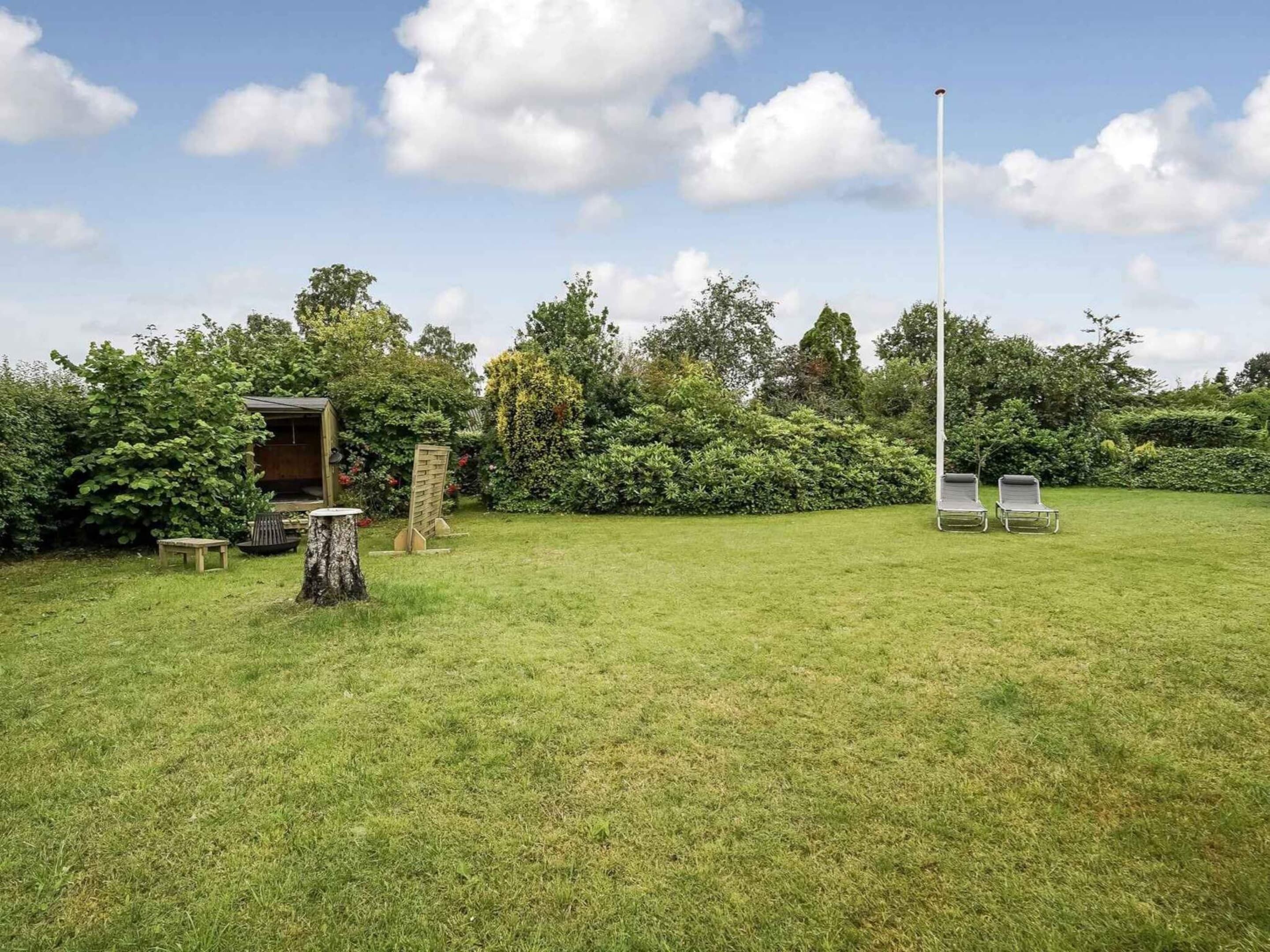 A grassy outdoor area with a wooden structure, a tall pole, and two lounge chairs.