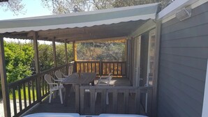 A covered outdoor deck with a hot tub, wooden chairs, and a table. - Camping 3 étoiles - Piscine (Arces)